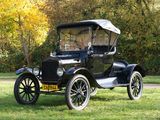 an old black car parked in a grassy field with trees in the background