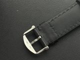 black leather watch strap with silver buckle laying on a black surface