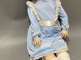 an old doll with blonde hair and blue dress sitting on a gray surface
