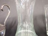 three glass vases and a silver pitcher on a table