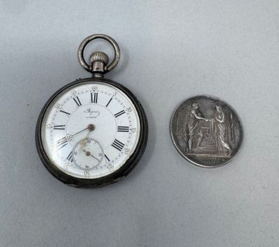 une petite montre de poche en argent à côté d'une pièce de dix cents