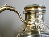a silver tea pot with a handle on a table