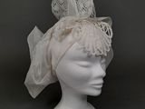 coiffe blanche ornée de dentelle et de plumes, posée sur une tête de mannequin