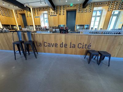 un bar avec des tabourets devant et une enseigne indiquant « Cave de la Cité »