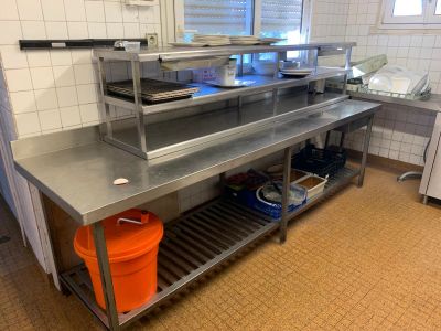 un grand plan de travail en inox dans une cuisine, avec des seaux orange posés par terre