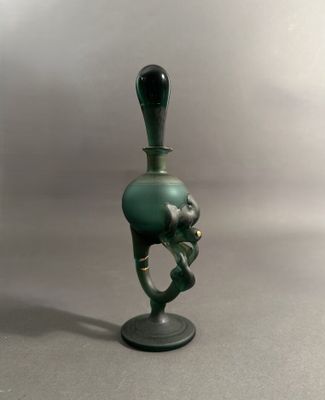 un vase en verre vert muni d'une anse noire, posé sur un socle