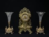 une horloge dorée et trois vases en verre sur fond noir