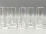 six tall clear glass vases lined up on a white surface