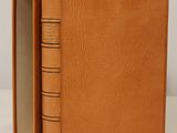 un livre en cuir marron dont trois pages sont ouvertes sur une surface blanche