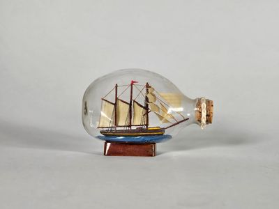 un petit bateau dans une bouteille en verre posée sur un socle en bois