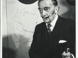 black and white photograph of a man in a suit sitting in front of a sign