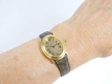 wrist shot of a woman wearing a gold wrist watch with a black leather band