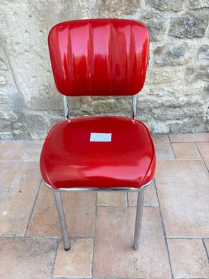 une chaise rouge avec une étiquette, posée devant un mur de pierre