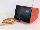 un petit téléviseur orange et un téléphone posés sur un plan de travail blanc