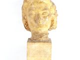 statue représentant la tête d'une femme, posée sur un socle en bois, sur fond blanc