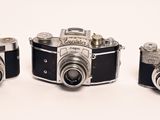 three old cameras sitting side by side on a white surface