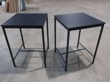 une paire de tables d'appoint en métal noir posées sur un sol en béton dans une zone d'entrepôt