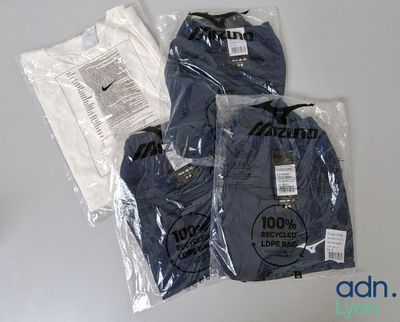trois t-shirts emballés dans des sacs en plastique, posés sur une table