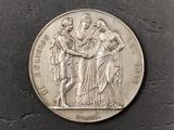 a silver coin with a woman and two men on it