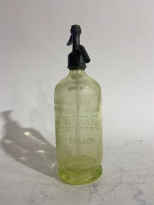 an old green glass bottle with a black cap on a white surface