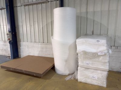 une pile de rouleaux de plastique blancs posée par terre à côté d'un carton