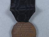 an old bronze medal with a black ribbon on a white surface