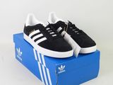 des baskets adidas noires et blanches posées sur une boîte bleue, sur fond blanc