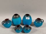 six small blue vases and two smaller blue vases on a white surface