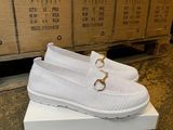 La boîte à chaussures est remplie de chaussures blanches ornées d'une boucle dorée.