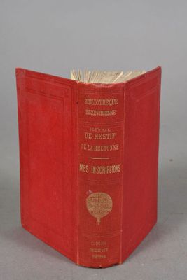 an old red book sitting on top of a table next to a gray wall