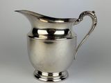 an antique silver plated pitcher with a curved handle