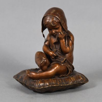 an antique bronze figurine of a child sitting on a pillow