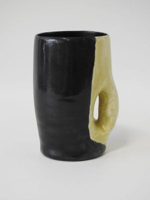 une tasse noire avec une anse jaune posée sur une table blanche
