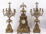 trois bougeoirs en laiton vieilli et une horloge sur fond blanc