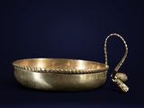 an antique brass bowl with a handle on a dark blue background