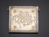 a silver plaque with arabic writing on a black background