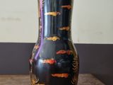 a black vase with gold fish on it sitting on a wooden table