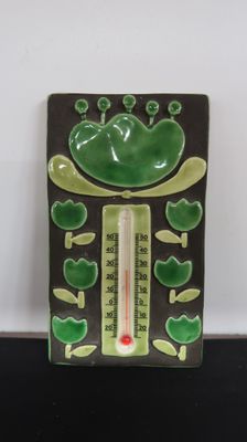 a green frog that is sitting on a thermometer