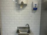 un lavabo dans des toilettes publiques, avec un distributeur de serviettes en papier fixé au mur
