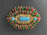 a close up of a broochle with a blue stone surrounded by green and red beads