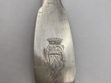 silver spoon with a crest on it sitting on a white surface