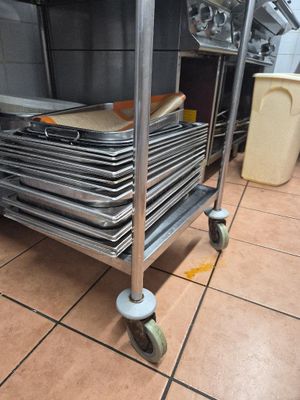 several trays of pans are stacked on a cart in a kitchen