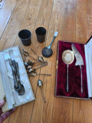une boîte contenant de l'argenterie posée sur un plancher en bois, à côté d'une paire de cuillères et de cuillères