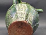 a green vase with a brown handle on a table