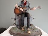 a statue of a man sitting on a rock playing a guitar
