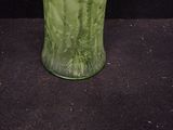 a green vase with flowers in it sitting on a black surface