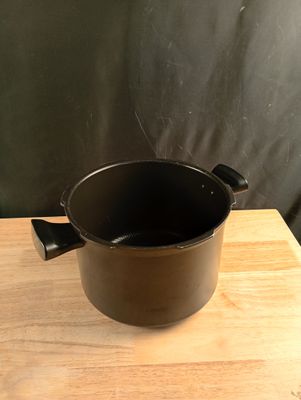 un pot noir posé sur une table en bois, avec un mur noir en arrière-plan