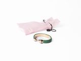 un bracelet vert et un sac rose posés sur une surface blanche