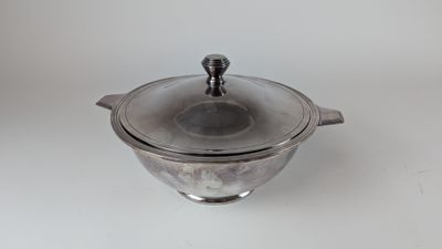 casserole plaquée argent avec couvercle en verre, posée sur un plan de travail blanc
