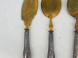 three silver and gold serving utensils on a white surface